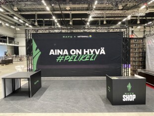 Aina on hyvä pelikeli -kangasbanderolli tapahtumassa.